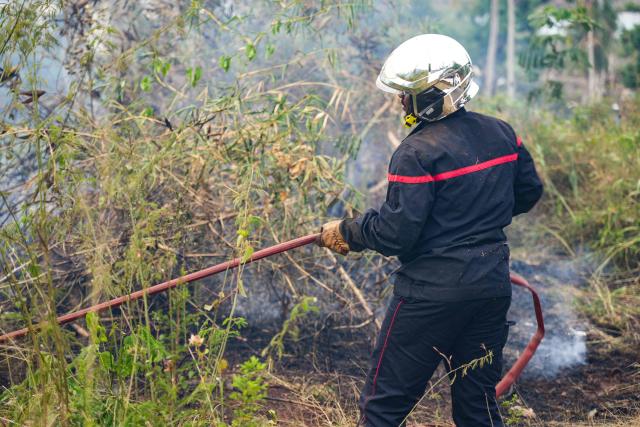 A firefighter works at extenguishing burning vegetation during a wildfire in the village of Ironi Be, in the township of Dembeni, on the French Indian Ocean territory of Mayotte on August 12, 2025. Since Cyclone Chido hit Mayotte on December 14, 2024, fires have been fueled by fallen vegetation. (Photo by Marine GACHET / AFP)