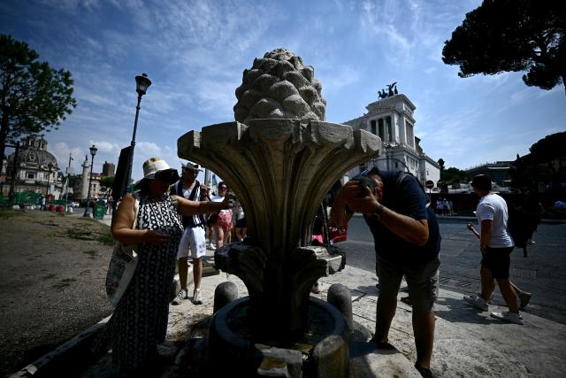 People drink water from the "fontana della Pigna" in Rome's Piazza Venezia on August 13, 2025. Italy is facing extreme heat until mid-August as temperatures above 40 degrees centigrade is gripping the entire country at least until the August 15th bank holiday weekend. (Photo by Filippo MONTEFORTE / AFP)