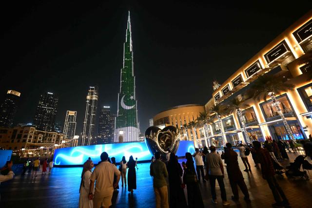 People look at Dubai's Burj Khalifa as it's lit up with the flag of Pakistan on August 14, 2025, to commemorate the 75th Independence Day of the South Asian country. (Photo by Giuseppe CACACE / AFP)