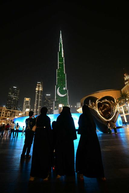 People look at Dubai's Burj Khalifa as it's lit up with the flag of Pakistan on August 14, 2025, to commemorate the 75th Independence Day of the South Asian country. (Photo by Giuseppe CACACE / AFP)