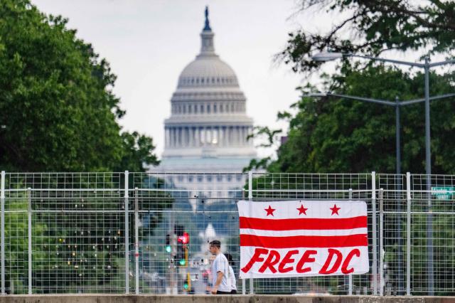 Pedestrians walk past a flag that reads “Free DC” hanging on an overpass near the US Capitol building in Washington, DC, on August 15, 2025. Attorney General of the District of Columbia Brian Schwalb has sued Donald Trump's administration over what he called a "hostile takeover" of the city's police force, which the Republican president said was necessary to fight violent crime. Earlier this week, Trump placed the capital's Metropolitan Police Department under federal government control while also sending 800 National Guard troops onto the city's streets. (Photo by Jim WATSON / AFP)