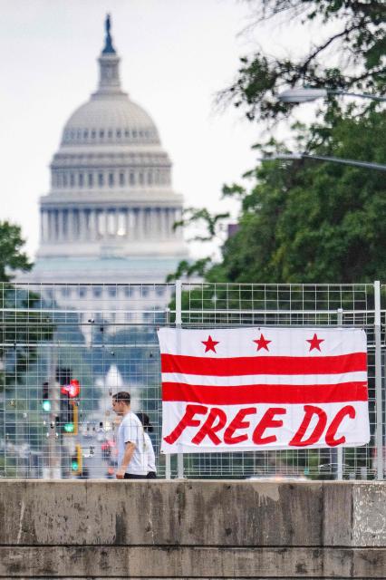 Pedestrians walk past a flag that reads “Free DC” hanging on an overpass near the US Capitol building in Washington, DC, on August 15, 2025. Attorney General of the District of Columbia Brian Schwalb has sued Donald Trump's administration over what he called a "hostile takeover" of the city's police force, which the Republican president said was necessary to fight violent crime. Earlier this week, Trump placed the capital's Metropolitan Police Department under federal government control while also sending 800 National Guard troops onto the city's streets. (Photo by Jim WATSON / AFP)