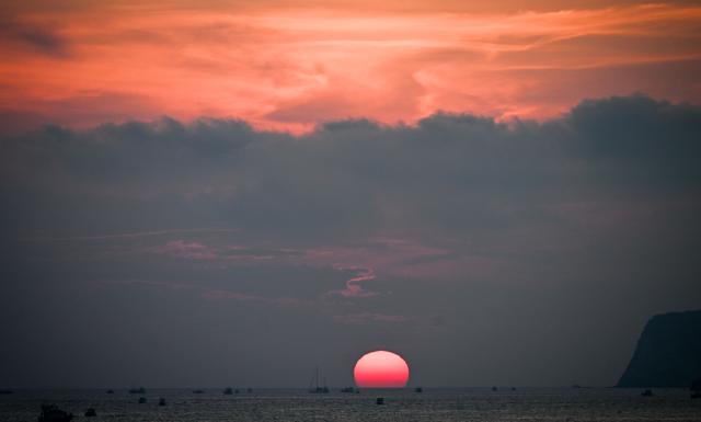Boats sail at sunset off the coast of Lampedusa, south Italy on August 15, 2025. (Photo by Stefano RELLANDINI / AFP)