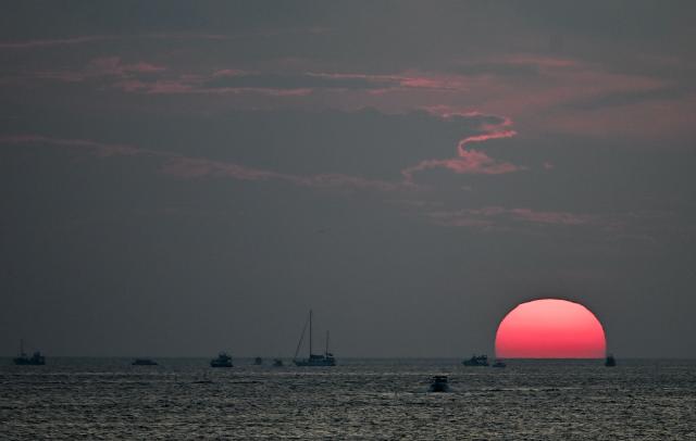 Boats sail at sunset off the coast of Lampedusa, south Italy on August 15, 2025. (Photo by Stefano RELLANDINI / AFP)