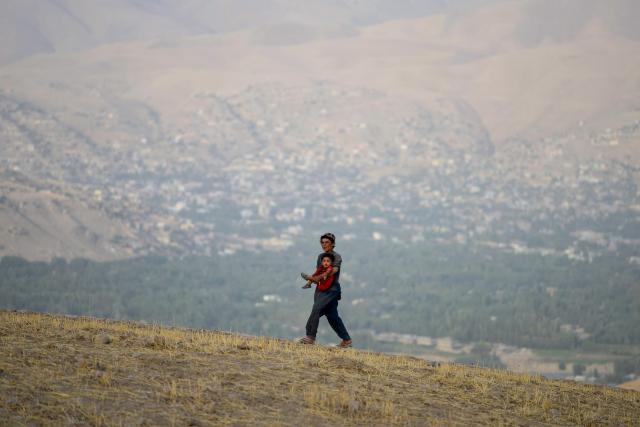 An Afghan boy carries a child as he walks across a hilltop in the Argo district of Badakhshan province on August 19, 2025. (Photo by Omer ABRAR / AFP)