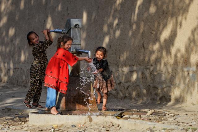 Afghan girls drink water from a handpump along a roadside in the Argo district of Badakhshan province on August 19, 2025. (Photo by Omer ABRAR / AFP)