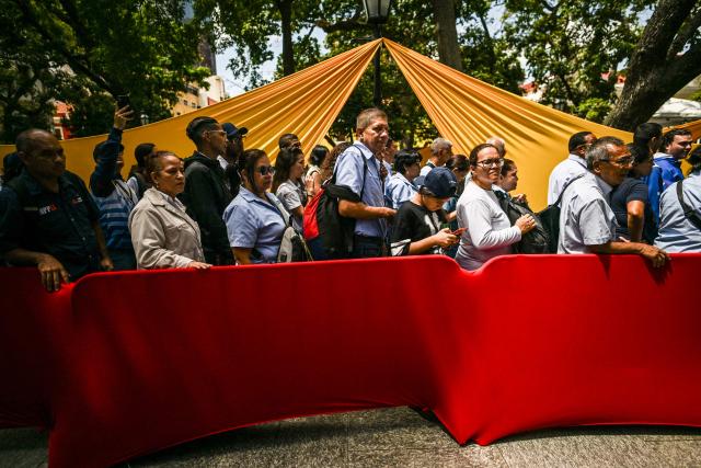 People line up during the Bolivarian militia enlistment process at Bolivar square in Caracas on August 23, 2025. Thousands of people enlisted in Venezuela's military forces on Saturday to join the ranks in preparation for a possible US invasion. (Photo by Juan BARRETO / AFP)