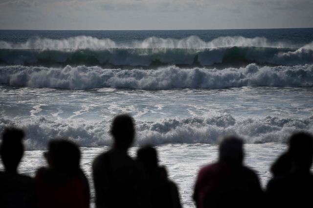 People watch as big waves, triggered by a cyclonic swell caused by former hurricane Erin and high tidal coefficients, crash on the beach in Lacanau, southwestern France on August 26, 2025. Meteo-France has placed six departments on yellow alert for wave and submersion. According to the meteorological institute, this phenomenon is expected to cause "waves of 4 to 5 meters on the Atlantic coasts and the entrance to the English Channel" and possible "local flooding, particularly at high tide," scheduled between 7:00 PM and 8:00 PM in the Nouvelle-Aquitaine region. (Photo by Christophe ARCHAMBAULT / AFP)
