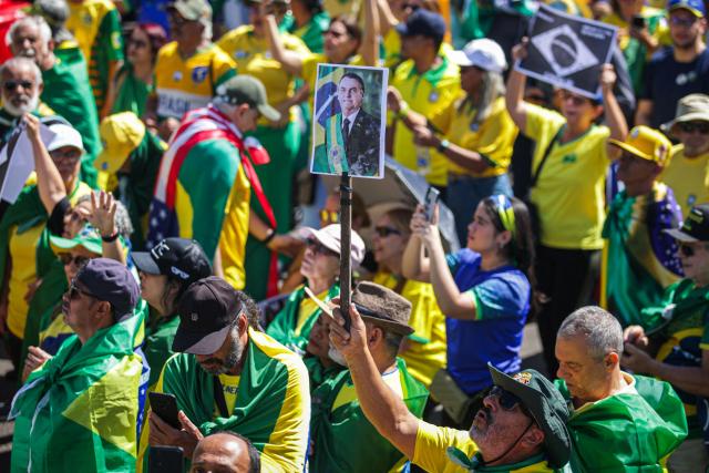 Supporters of Brazil's former president (2019-2022) Jair Bolsonaro, on trial for his alleged role in an attempted coup, hold signs during a demonstration during Independence Day, in Brasilia on September 7, 2025. Bolsonaro will test his political strength with demonstrations in the country's main cities, days before the Supreme Court deliver its verdict. The far-right leader, also a former army captain, risks up to 43 years in prison if convicted of attempting to cling to power after losing 2022 elections to his leftist rival Luiz Inacio Lula da Silva. (Photo by Arthur Menescal / AFP)