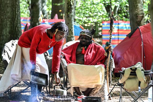 'King Atehene' (R), and handmaiden 'Asnat' (L) from the 'Kingdom of Kubala' sit around their fire at their camp near Jedburgh in the Scottish Borders on September 8, 2025 on what they say is their ancestral land. 'King Atehene', 'Queen Nandi' and their handmaiden 'Asnat' have set up camp near Jedburgh claiming land that they say belonged hundreds of years ago to the 'Kingdom of Kubala'. Local residents have been bringing supplies to help the three after their first camp was reportedly destroyed. The group have reportedly recieved a notice of eviction by the council. (Photo by Andy Buchanan / AFP)