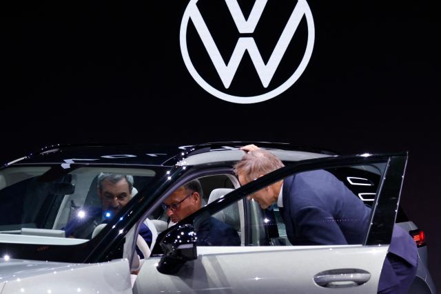 Oliver Blume, CEO of the Volkswagen Group (R) looks on as German Chancellor Friedrich Merz (C) and Bavaria's State Premier Markus Soeder (L) gets into a VW ID Cross concept car at the VW booth, during the opening day of the International Motor Show IAA on September 9, 2025, in Munich, southern Germany. The IAA Mobility fair runs from September 9 to 14, 2025. (Photo by Alexandra BEIER / AFP)