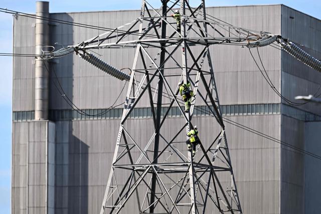 Workman work on the electricity pylons and power lines at Heysham Nuclear Power Station in Heysham, on the north west coast of England on September 9, 2025. Two British nuclear power plants nearing the end of their lifespan will run for an extra year, its operators announced last week, helping with UK energy security and net zero targets. The Heysham 1 plant in northwest England and the Hartlepool facility in the northeast will continue generating energy until March 2028, an increase of one year, main operator EDF said in a statement. (Photo by Paul ELLIS / AFP)