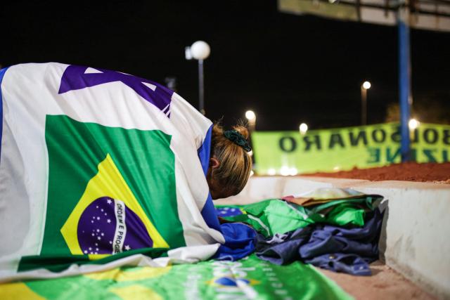 A supporter of Brazil's former President Jair Bolsonaro covered with an Israeli flag prays near his residence in Brasilia on September 9, 2025. Bolsonaro, 70, risks a prison term of over 40 years if found guilty of seeking to stay in power after his defeat in 2022 elections to leftist Luiz Inacio Lula da Silva. (Photo by Arthur MENESCAL / AFP)
