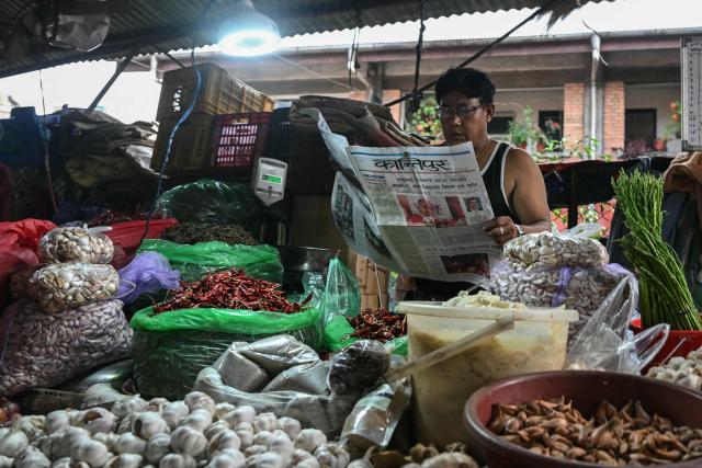 A vegetable vendor reads a Nepali-language newspaper on a roadside in Kathmandu on September 12, 2025, featuring the country's former chief justice Sushila Karki with headlines related to ongoing unrest in Nepal. Nepal's president and army sought on September 12 to find a consensus interim leader to fill a political vacuum after deadly anti-corruption protests toppled the government and left parliament in flames. (Photo by Arun SANKAR / AFP)