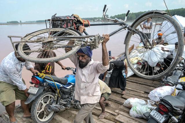 In this photograph taken on September 11, 2025, a villager unloads his bicycle after crossing the overflowing Ravi River on a boat following heavy monsoon rains in the village of Toor near the Gurdaspur district in India's Punjab state. The fields are full but the paddy brown and wilted, and the air thick with the stench of rotting crops and livestock -- the aftermath of record monsoon rains that have devastated India's breadbasket. (Photo by Narinder NANU / AFP) / To go with 'India-Pakistan-Flood-Climate-Agriculture', FOCUS by Arunabh SAIKIA