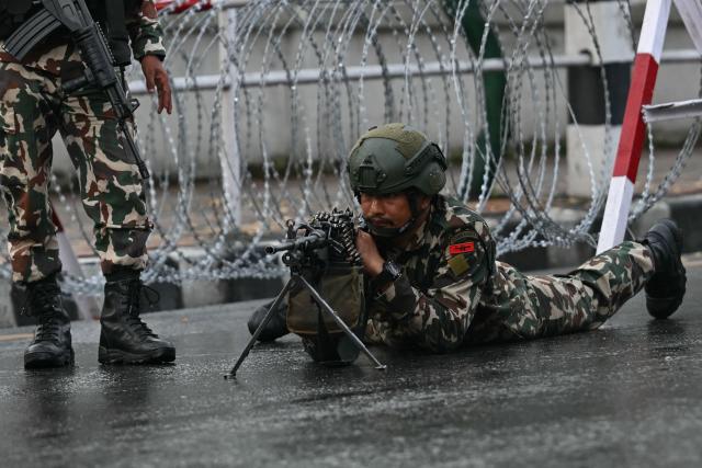 Nepal's army soldier takes his position to disperse the protesters in front of the President House during a curfew imposed to restore law and order, in Kathmandu on September 12, 2025. Nepal's president and army sought on September 12 to find a consensus interim leader to fill a political vacuum after deadly anti-corruption protests toppled the government and left parliament in flames. (Photo by Arun SANKAR / AFP)