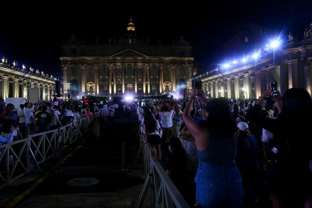 Spectators take photographs with their mobile phones during the "Grace for the World" free concert and light show in Saint Peter's Square at the Vatican on September 13, 2025. "Grace for the World" concert is co-directed by American songwriter Pharrell Williams and Italian tenor Andrea Bocelli. The event marks the end of the third "World Meeting on Human Fraternity", a series of encounters launched after the 2020 publication of the "All Brothers" encyclical by the late pope Francis. (Photo by Filippo MONTEFORTE / AFP)