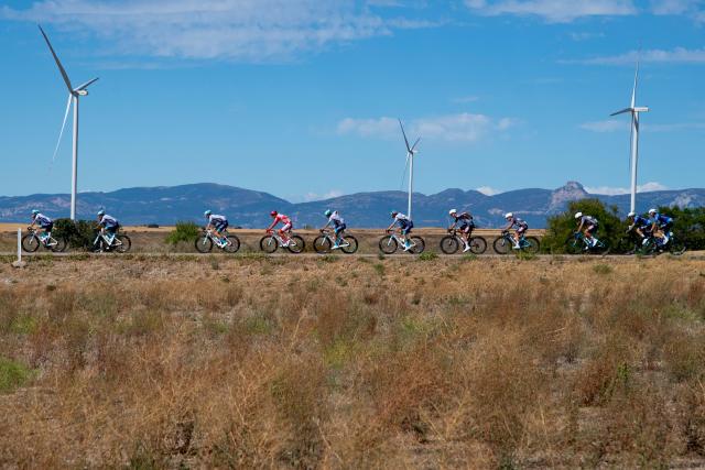 The pack rides past wind turbines during the 8th stage of the Vuelta a Espana, a 158 km race between Monzon Templario and Zaragoza, on August 30, 2025. (Photo by Josep LAGO / AFP)