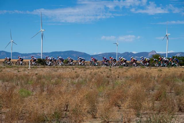The pack rides past wind turbines during the 8th stage of the Vuelta a Espana, a 158 km race between Monzon Templario and Zaragoza, on August 30, 2025. (Photo by Josep LAGO / AFP)