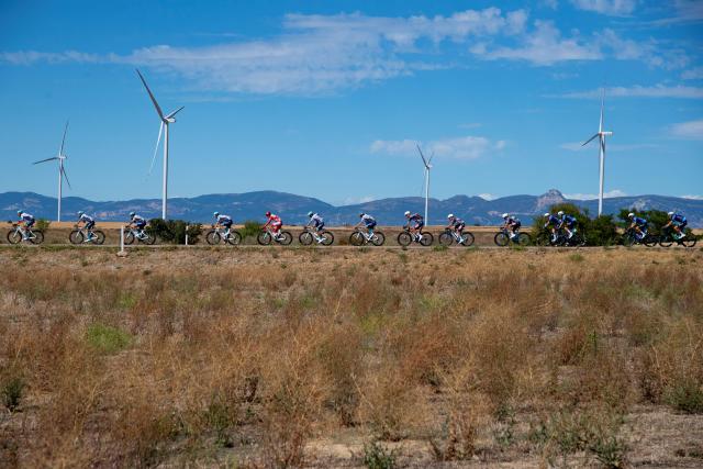 The pack rides past wind turbines during the 8th stage of the Vuelta a Espana, a 158 km race between Monzon Templario and Zaragoza, on August 30, 2025. (Photo by Josep LAGO / AFP)