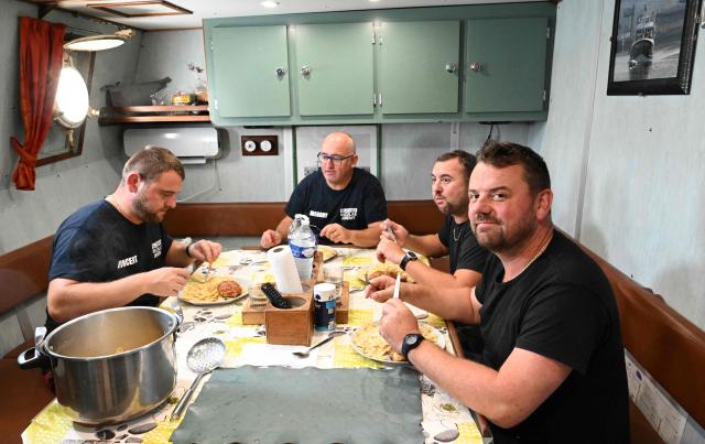 Crew members of the trawler "Nicolas-Jeremy", which practices pair trawling in tandem with the "Notre Dame de Boulogne" trawler, eat a meal during a sardine fishing campaign, off the Baie de Somme of northern France, on September 8, 2025. Between regulations, the creation of non-fishing zones, licenses to access to British waters and possible competition from some North Sea countries, the captain of the "Nicolas-Jeremy" fears his generation could the last of a long line of fishermen. (Photo by FRANCOIS NASCIMBENI / AFP)