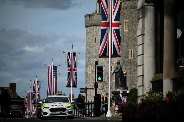 A police car drives past US and Union Jack flags flying from poles outside Windsor Castle in Windsor, on September 16, 2025, on the eve of a State Visit by the US President and the First Lady. Donald Trump lands in Britain on Tuesday for an historic second state visit that will see the UK government spare no effort in trying to flatter the mercurial American president. (Photo by JUSTIN TALLIS / AFP)