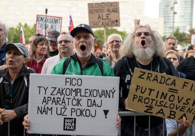 A participant (L) holds a placard reading 'Fico you complexed Apparatchik leave us alone' while protesting against the government's proposed cost-cutting measures during a rally against nationalist premier Fico in Bratislava on September 16, 2025. Since his return to power in 2023, Fico has faced a series of protests over his curbing of rights and seeking close ties with Russian President Putin. Thousands of Slovaks gathered in front of the government's main office building in Bratislava, shouting "Enough of Fico! Fico go to jail!" and "It is enough. We are fed up!" The protest was called by the opposition, with organisers estimating up to 18,000 people attended. (Photo by Joe Klamar / AFP)