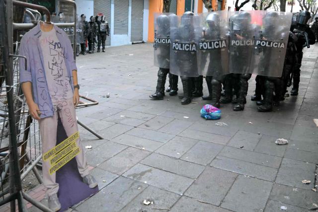 Ecuadorian riot police officers stand guard in front of a cardboard depicting President Daniel Noboa during a protest against the government's cuts and the elimination of diesel subsidy within a state of emergency in Quito on September 16, 2025. (Photo by Rodrigo BUENDIA / AFP)