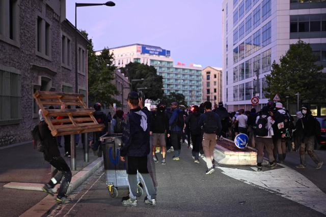 People gather as others carry items to build a barricade in Marseille, southeastern France, on September 18, 2025, ahead of a road blocage as part of a day of nationwide strikes and protests called by unions over France's national budget. France is bracing for a day of nationwide protests on September 18, 2025, with a source close to the authorities saying some 800,000 people are expected to take to the streets. In a rare show of unity, trade unions have urged French people to strike in protest at the authorities' "horror show" draft budget designed to reduce France's ballooning debt. (Photo by Miguel MEDINA / AFP)