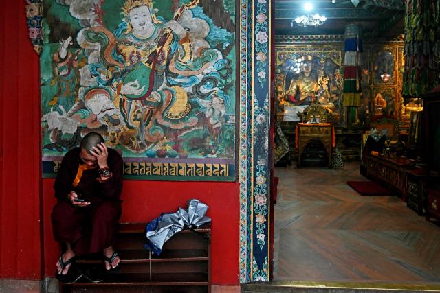 A Buddhist monk checks his phone whilst he sits at Boudhanath Stupa in Kathmandu on September 18, 2025. (Photo by Arun SANKAR / AFP)