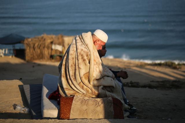 An elderly man and a child sit by the beach as displaced Palestinians move with their belongings (not in the picture) southwards, on a road in the Nuseirat refugee camp area in the central Gaza Strip, following renewed Israeli evacuation orders for Gaza City on September 18, 2025. Israel has announced a major ground assault in Gaza City that it says is aimed at crushing Hamas in the Palestinian territory's largest urban hub. (Photo by Eyad BABA / AFP)