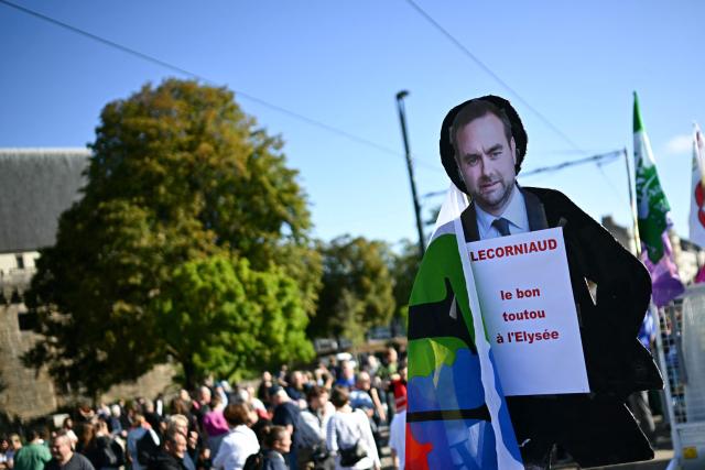 Protesters hold a placard depicting France's newly appointed Prime Minister Sebastien Lecornu reading a slogan with a play on words on his surname and followed by "the good doggy of the Elysee" as they take part in demonstration in Nantes, western France, on September 18, 2025, during a day of nationwide strikes and protests called by unions over France's national budget. France is bracing for a day of nationwide protests on September 18, 2025, with a source close to the authorities saying some 800,000 people are expected to take to the streets. In a rare show of unity, trade unions have urged French people to strike in protest at the authorities' "horror show" draft budget designed to reduce France's ballooning debt. (Photo by Loic VENANCE / AFP)