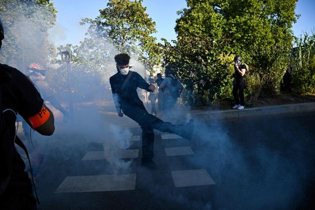 A protestor kicks a teargas canister fired by French police in Paris, on September 18, 2025, during a day of nationwide strikes and protests called by unions over France's national budget. France is bracing for a day of nationwide protests on September 18, 2025, with a source close to the authorities saying some 800,000 people are expected to take to the streets. In a rare show of unity, trade unions have urged French people to strike in protest at the authorities' "horror show" draft budget designed to reduce France's ballooning debt. (Photo by JULIEN DE ROSA / AFP)