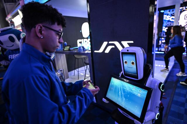 A young man interacts with a robot during the communications and technology fair in Caracas on September 18, 2025. (Photo by Juan BARRETO / AFP)