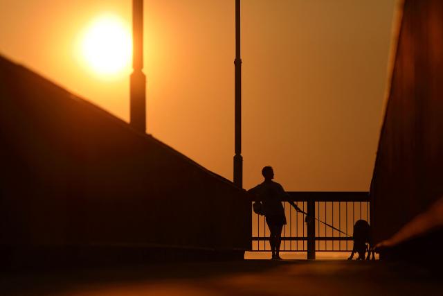 This picture taken on September 22, 2025, shows a man walking his dog across a bridge as the sun sets over Leighton Beach in Perth. (Photo by Antony DICKSON / AFP)