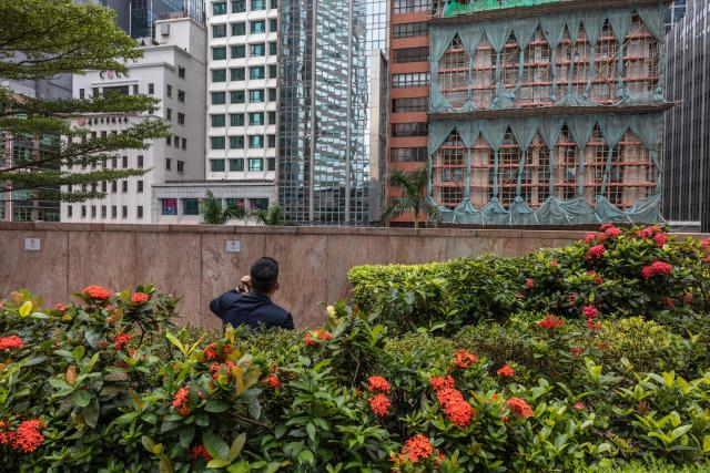 A man talks on his phone in front of a building under renovation covered with bamboo scaffolding and the netting tied up in preparation for Super Typhoon Ragasa in Hong Kong on September 23, 2025. Hong Kong shut schools and cancelled flights on September 23 as Super Typhoon Ragasa was set to slam into the financial centre with a force that officials warned would be among the most destructive in the city's recent history. (Photo by Dale DE LA REY / AFP)