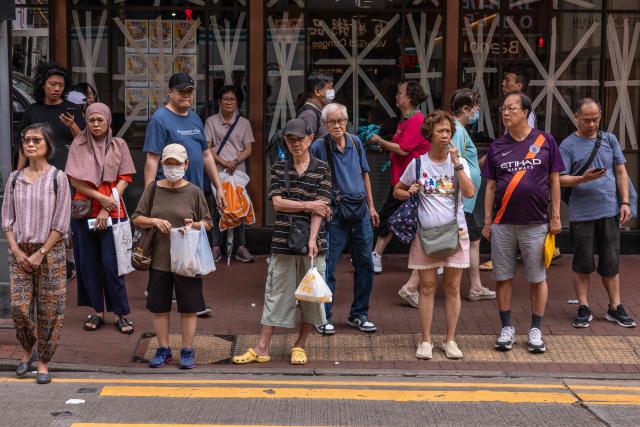 People wait to cross a street in front of a restaurant with taped windows as Super Typhoon Ragasa moved towards Hong Kong on September 23, 2025. Hong Kong shut schools and cancelled flights on September 23 as Super Typhoon Ragasa was set to slam into the financial centre with a force that officials warned would be among the most destructive in the city's recent history. (Photo by Dale DE LA REY / AFP)