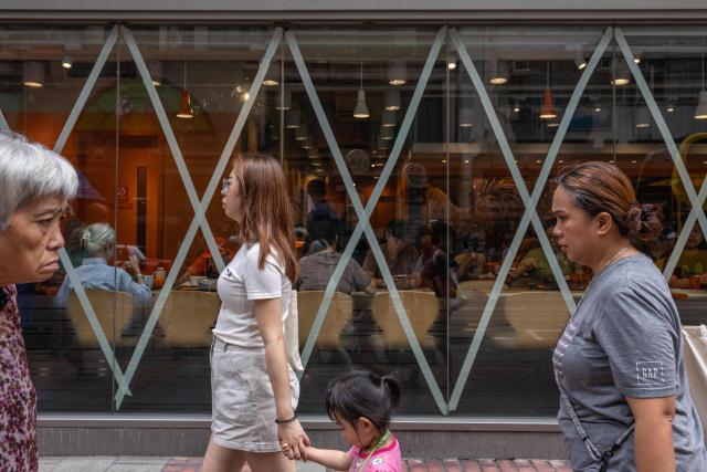 People walk past a restaurant with taped windows as Super Typhoon Ragasa moved towards Hong Kong on September 23, 2025. Hong Kong shut schools and cancelled flights on September 23 as Super Typhoon Ragasa was set to slam into the financial centre with a force that officials warned would be among the most destructive in the city's recent history. (Photo by Dale DE LA REY / AFP)