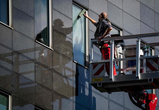 A window cleaner on a mobile lift is reflected in a glass facade as he plies his trade in Berlin's Mitte district on September 23, 2025. (Photo by John MACDOUGALL / AFP)