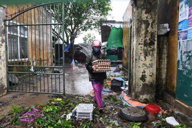 A woman carries belongings as she walks amidst the debris after typhoon Bualoi made a landfall in Nghe An province on September 29, 2025. Vietnam said it evacuated almost 30,000 residents from coastal areas on September 28, as Typhoon Bualoi hit the country's steel-producing central belt. (Photo by Thai An / AFP)