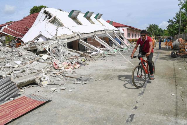 TOPSHOT - A man rides a bicycle past a collapsed building where three missing people were found dead among the rubbles in Bogo City, Cebu province on October 2, 2025, in the aftermath of a 6.9-magnitude quake that struck off the coast of the central Philippines late September 30. The death toll from a powerful earthquake in the central Philippines rose to 72 on October 2, rescuers said, as officials turned their efforts to the hundreds injured and thousands left homeless. (Photo by Ted ALJIBE / AFP)