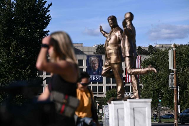 A photo of Donald Trump hanging on the facade of the Labor Department with the words "American Workers First" is seen in the distance near a statue depicting US President Donald Trump and Jeffrey Epstein holding hands by the US Capitol on October 2, 2025 in Washington, DC. A statue titled "Best Friends Forever" by the anonymous art collective "The Secret Handshake" was installed near the US Capitol on September 23 and removed by the National Park Service the following day. The sculpture has now mysteriously reappeared on October 2. (Photo by Brendan SMIALOWSKI / AFP)