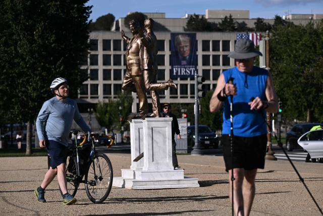 A photo of Donald Trump hanging on the facade of the Labor Department with the words "American Workers First" is seen in the distance near a statue depicting US President Donald Trump and Jeffrey Epstein holding hands by the US Capitol on October 2, 2025 in Washington, DC. A statue titled "Best Friends Forever" by the anonymous art collective "The Secret Handshake" was installed near the US Capitol on September 23 and removed by the National Park Service the following day. The sculpture has now mysteriously reappeared on October 2. (Photo by Brendan SMIALOWSKI / AFP)