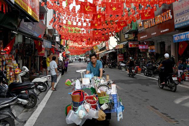 A street vendor pushes his cart under flags of Vietnam and the country's Communist Party in Hanoi on October 3, 2025. (Photo by Nhac NGUYEN / AFP)