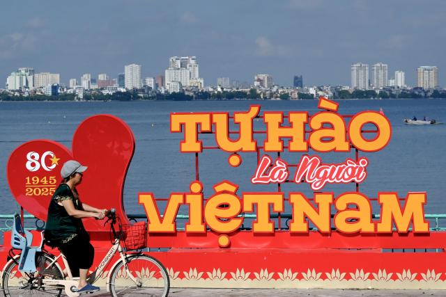 A woman cycles past a sign reading "Proud to be Vietnamese" on the banks of West Lake in Hanoi on October 3, 2025. (Photo by Nhac NGUYEN / AFP)