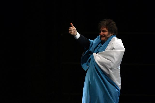 Argentina's President Javier Milei gives a thumbs-up while wrapped in the Argentine flag during the launch of his new book, "The Making of the Miracle," at the Movistar Arena in Buenos Aires on October 6, 2025. (Photo by Luis ROBAYO / AFP)