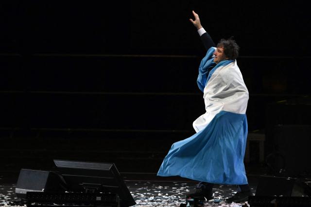 Argentina's President Javier Milei greets supporters while wrapped in the Argentine flag during the launch of his new book, "The Making of the Miracle," at the Movistar Arena in Buenos Aires on October 6, 2025. (Photo by Luis ROBAYO / AFP)