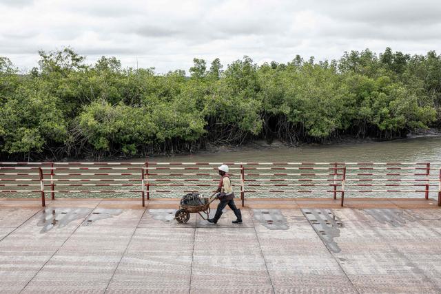 (FILES) A SimFer employee pushes a wheelbarrow at the Morebaya Port in Forecariah, on September 4, 2025. The Simandou mining project is expected to start iron ore production in November 2025, almost 30 years after explorations began in the Simandou mountain range. In the Simandou mountains of Guinea's lush rainforest, a mammoth mining project that could make the west African country one of the world's largest iron exporters is raising equal parts hope and fear.
In just a few weeks, Guinea will export its first shipments of iron ore from its Simandou Project, finally cashing in on the high-grade iron deposits discovered decades ago in the country's southeast.
Not only does the project potentially offer a steady stream of revenue for the impoverished country but it has also precipitated the development of key infrastructure in the region, although the opacity of contracts make it impossible to estimate the state's gains.
Industrial partners have spent approximately $20 billion constructing more than 650 kilometres (400 miles) of railway and a massive port that will connect the remote region to the larger world. (Photo by PATRICK MEINHARDT / AFP)