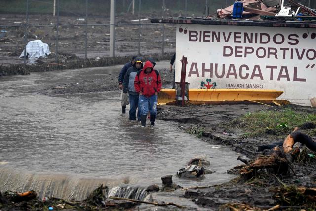 People wade through a flooded street due to the rains in the municipality of Huauchinango, Puebla State, Mexico on October 11, 2025. The death toll from heavy rains in Mexico rose to 37 on Saturday after nine more fatalities were confirmed, the Mexican government reported. (Photo by Alfredo ESTRELLA / AFP)