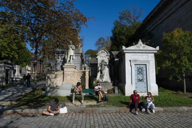 Visitors sit next to graves and statues enjoying a warm autumn day at the Pere Lachaise cemetery park in Paris on October 12, 2025. (Photo by Martin LELIEVRE / AFP)